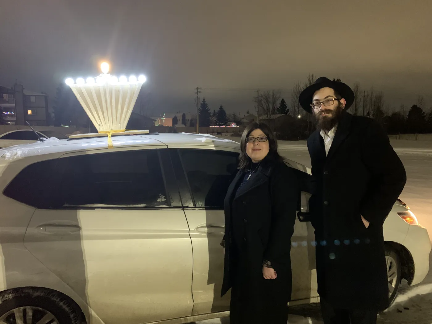 Where it started, 2019: Menachem and Shoshana Drelich beside the car with a lit menorah on a snowy night in Red Deer, Alberta